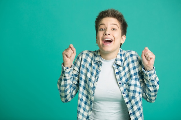 schöne junge Frau mit kurzen Haaren in einem Hemd an einer blauen Wand