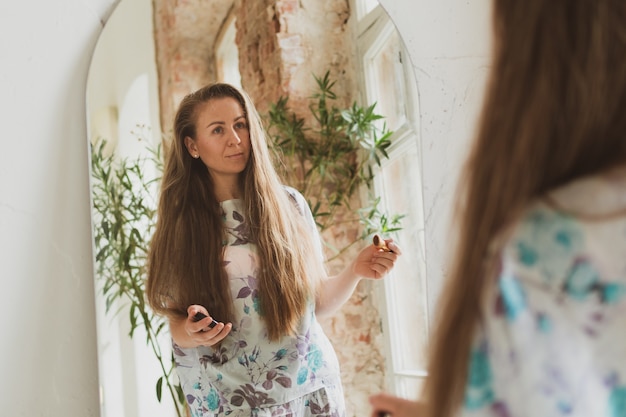 Foto schöne junge frau mit langen haaren, die ihr haar kämmt und in der nähe des spiegels make-up aufträgt