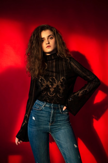 Foto schöne junge frau mit make-up und lockigem haar, gekleidet in einer schwarzen bluse und jeans, isoliert auf rotem hintergrund