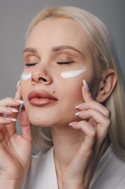 Schöne junge Frau mit natürlichem Make-up, die Creme auf ihrem frischen Gesicht aufträgt Gesichtspflege Gesichtsbehandlung Kosmetologie Schönheit und Spa