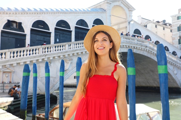 Schöne junge Frau mit rotem Kleid steht vor der berühmten Rialtobrücke in Venedig, Italien