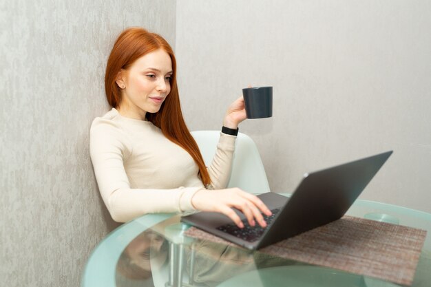 schöne junge Frau mit roten Haaren am Tisch mit einem Laptop