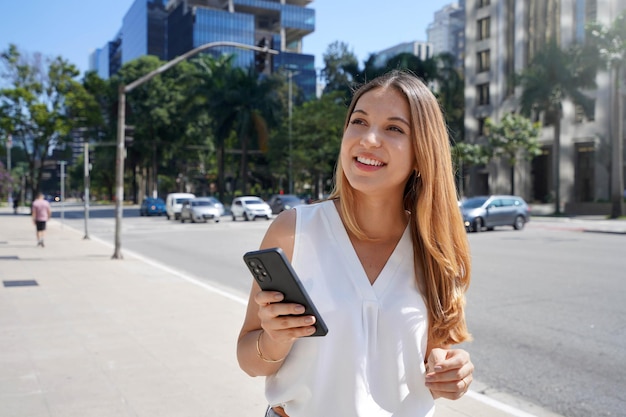 Schöne junge Frau mit Smartphone zu Fuß im Finanzviertel Portrait von wunderschönen lächelnden Frauen mit Handy in der modernen Metropole