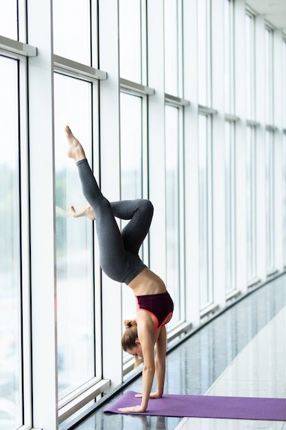 Schöne junge Frau mit Sport, der drinnen arbeitet, Yoga-Übung auf Matte machend,