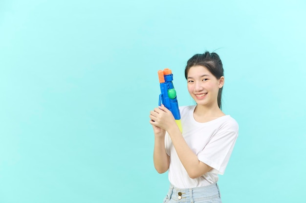 Schöne junge Frau mit Wasserpistole beim Songkran Festival Thailand isoliert auf blauem Hintergrund.