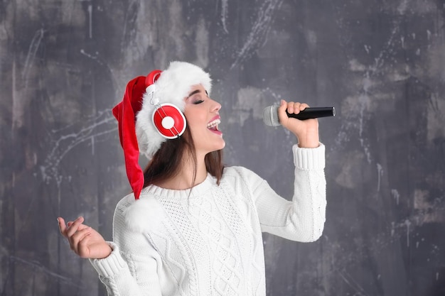 Schöne junge Frau mit Weihnachtsmütze singt Weihnachtslieder auf Grunge-Hintergrund