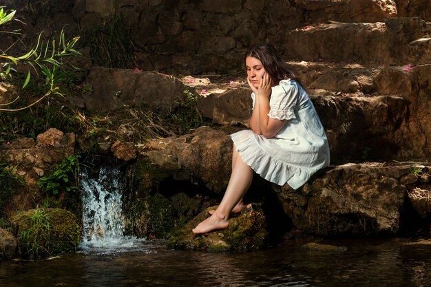 Schöne junge Frau mit weißem Kleid nahe Wasserstrom.