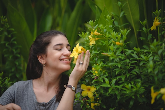 Schöne junge Frau mit zahnigem Lächeln, die schöne gelbe Blume fühlt und riecht, während sie in der Natur genießt und sich entspannt