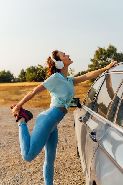 Schöne junge Frau mittleren Alters mit Helmen, die sich auf das Auto stützen und Dehnung tun. gesundes Lifestyle-Konzept. sport.selbstpflege