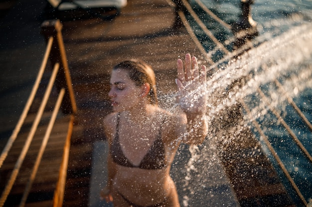 Schöne junge frau nimmt an einem sonnigen tag im freien am meer eine entspannende dusche in einem badeanzug. das mädchen im urlaub ruht sich aus. selektiver fokus