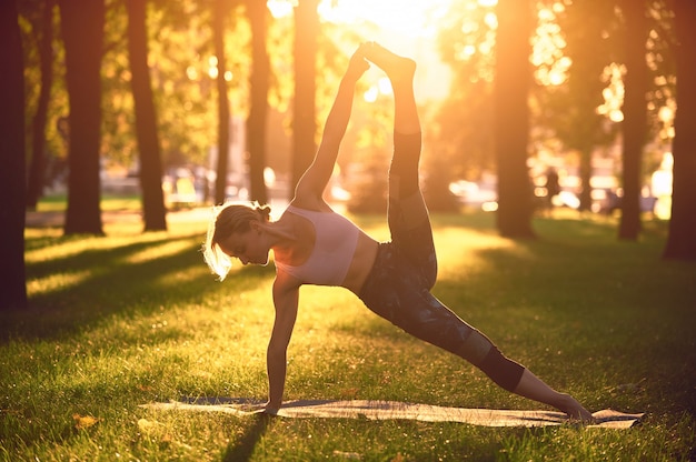 Schöne junge Frau praktiziert Yoga fortgeschrittene Seitenplanke Pose Vasisthasana im Park bei Sonnenuntergang