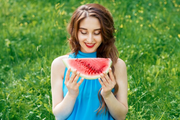 Schöne junge Frau schaut auf die Wassermelone, um im sonnigen Sommertag zu essen.