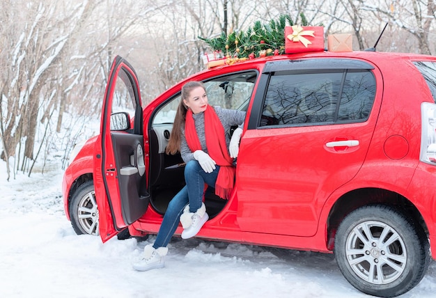 Schöne junge Frau sitzt im roten Auto, das für Weihnachten im Winterwald während Weihnachten dekoriert ist und