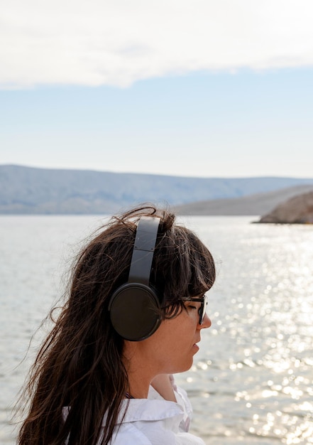 Schöne junge Frau steht am Strand und hört Musik mit Kopfhörern