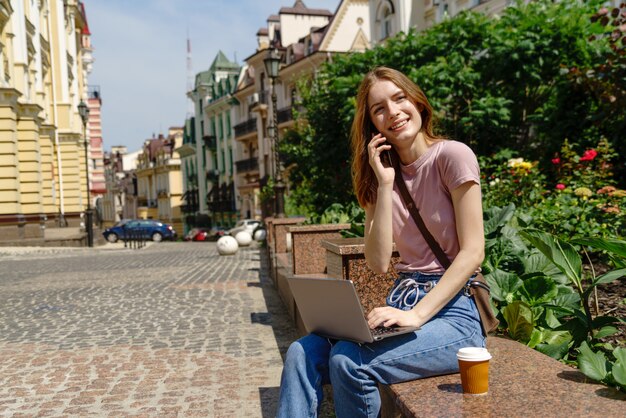 Schöne junge Frau Tourist mit Kaffee zum Mitnehmen im Stadtzentrum mit Laptop.