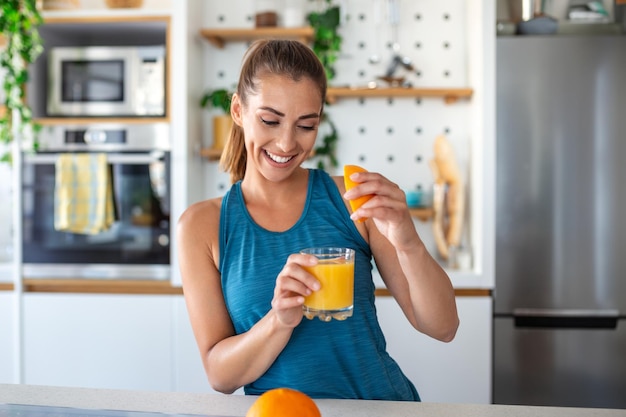 Schöne junge Frau trinkt frischen Orangensaft in der Küche, gesunde Ernährung, glückliche junge Frau.