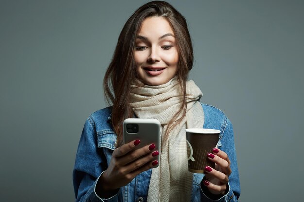 Schöne junge Frau trinkt Kaffee und schaut auf den Telefonbildschirm