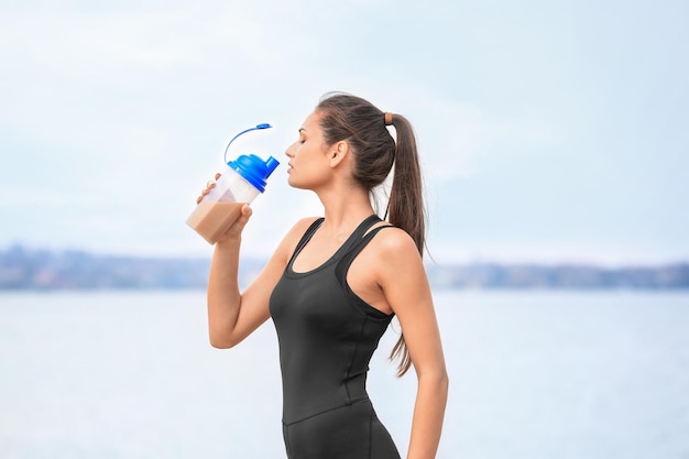 Schöne junge Frau trinkt Proteinshake am Flussufer