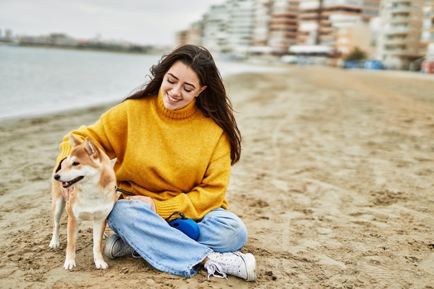 Schöne junge Frau umarmt einen glücklichen Shiba-Inu-Hund am Strand