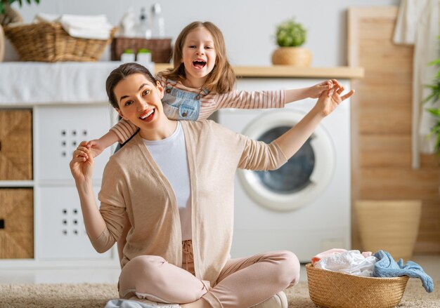 Schöne junge Frau und kleiner Helfer des Kindermädchens haben Spaß und lächeln beim Wäschewaschen zu Hause.