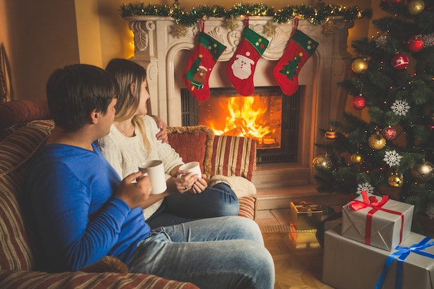 Schöne junge Frau und Mann entspannen am Kamin und geschmückten Weihnachtsbaum