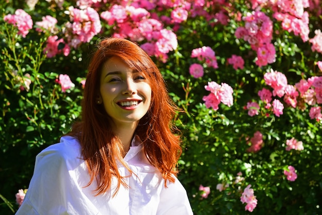 Schöne junge Frau wirft auf Hintergrund der roten Rosenblumen auf. Outdoor-Porträt einer schönen Frau.