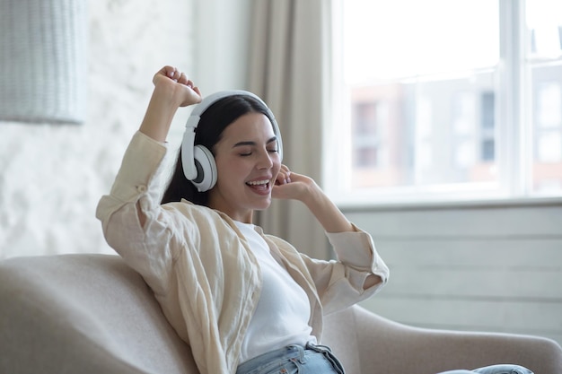 Schöne junge Frau zu Hause, die sich beim Musikhören über weiße Kopfhörer auf dem Sofa entspannt