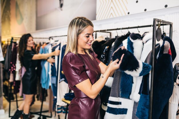 Schöne junge Frauen, die elegante Kleidung in einer teuren Boutique oder einem Geschäft ausprobieren.