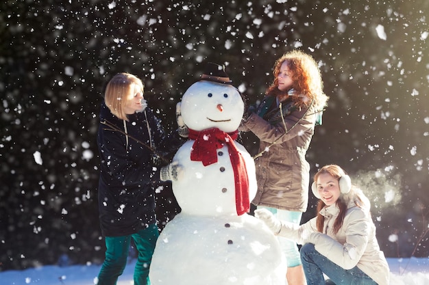 Schöne junge Frauen, die Spaß daran haben, an einem verschneiten Wintertag in einem Park einen Schneemann zu bauen