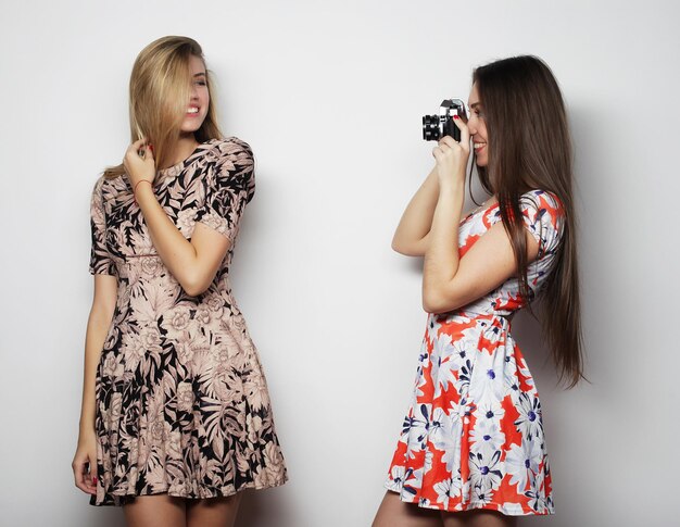 Schöne junge Frauen in Sommerkleidern werden auf einem weißen Hintergrund einer alten Kamera fotografiert