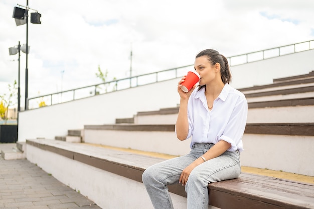 Schöne junge Frauen trinken Kaffee aus Pappbecher und genießen den sonnigen Tag in der Stadttreppe