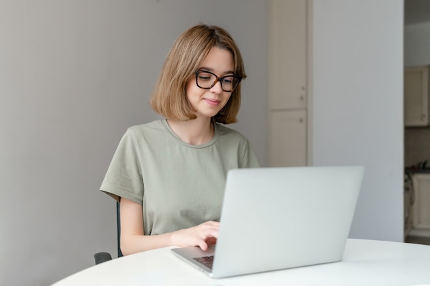 Schöne junge Freiberuflerin, die Laptop-Computer verwendet, der zu Hause sitzt. Online-Bildungskonzept