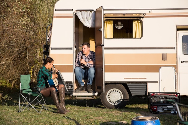 Schöne junge Freundin, die für ihren Freund vor ihrem Retro-Wohnmobil singt. Glückliches Paar.