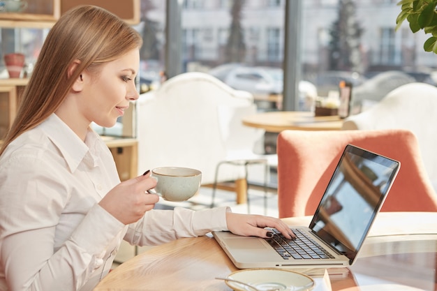 Schöne junge Geschäftsfrau, die den Kaffee, arbeitend an Laptop am Café genießt