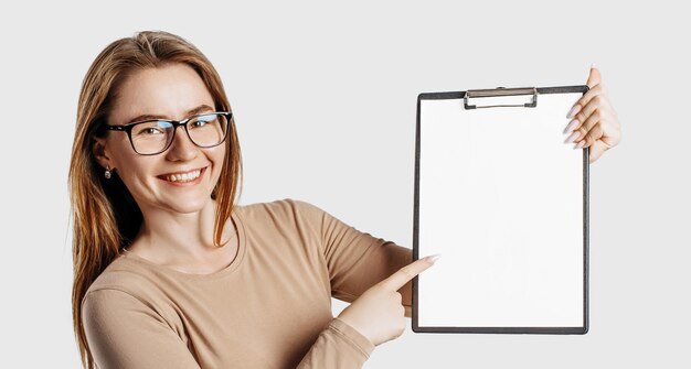 Schöne junge Geschäftsfrau, die eine Brille trägt, hält eine Zwischenablage mit Mock-up-Leerzeichen, die auf grauem Hintergrund isoliert sind. Erzielen von Karriere-Reichtum-Geschäftskonzept Online-Lernabdeckung