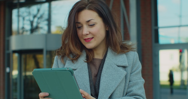 Schöne junge Geschäftsfrau mit Tablet außerhalb des Bürogebäudes.