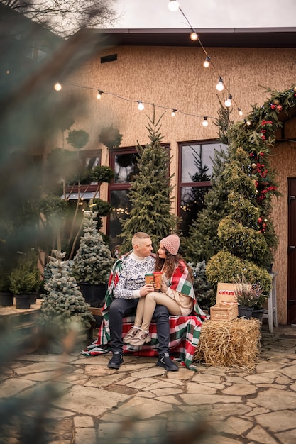 Foto schöne junge glücklich lächelnde paar in eine schottische decke gehüllt grüne weihnachtsbäume auf dem hintergrund die winterferien warten auf das neue jahr