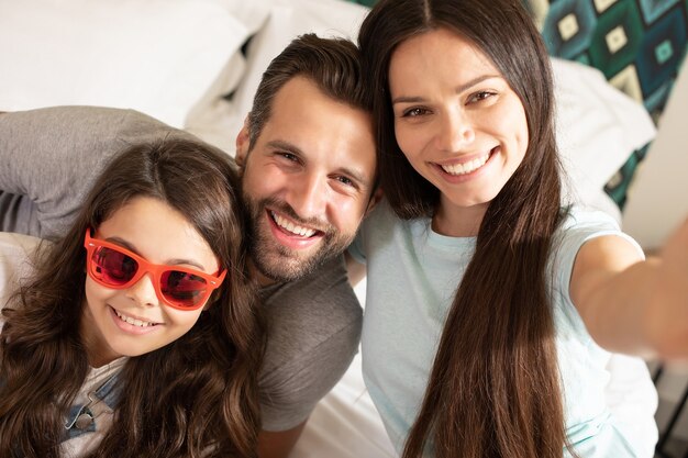 Schöne junge glückliche Familie, die selfie Foto im Schlafzimmer macht und Spaß zusammen hat