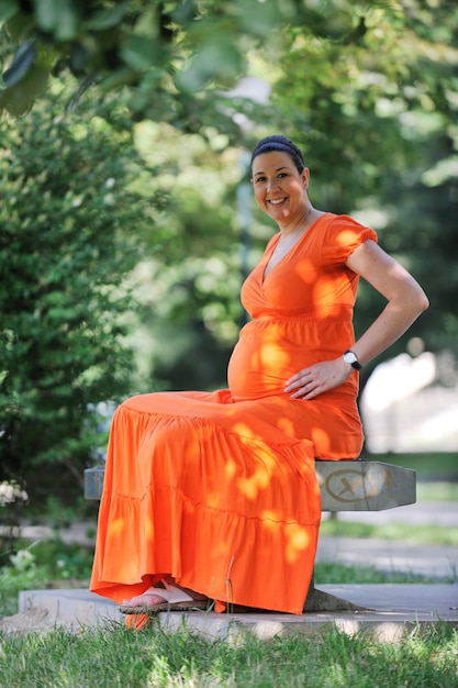 schöne junge glückliche schwangere Frau im Freien in heller Natur in orangefarbenem Kleid