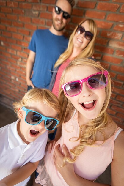 Foto schöne junge kaukasische bruder und schwester mit sonnenbrille und eltern hinter sich