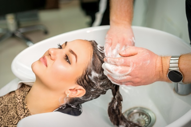 Schöne junge kaukasische Frau bekommt Haarwäsche durch männliche Hände des Friseurs im Friseursalon