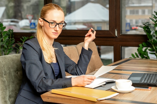 Schöne junge kaukasische Geschäftsfrau, die mit Dokumenten in einem Café arbeitet