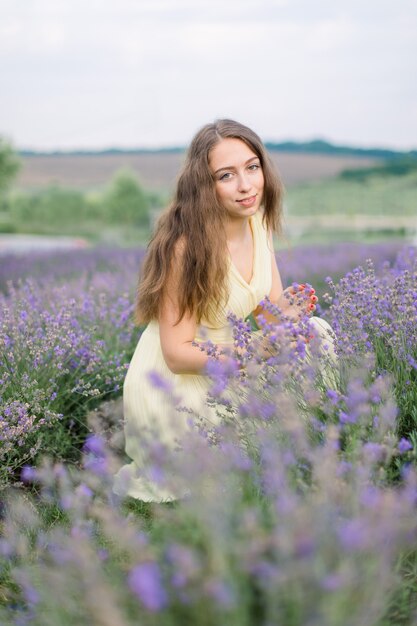 Schöne junge kaukasische langhaarige Frau in einem hellgelben Kleid sammelt Lavendel.