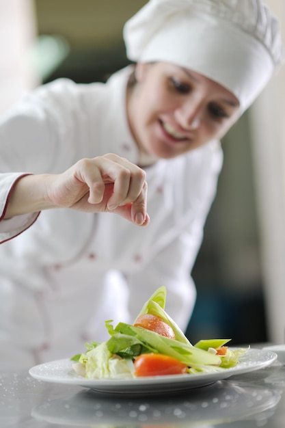 Schöne junge Köchin bereitet leckeres Essen in der Küche zu und dekoriert es