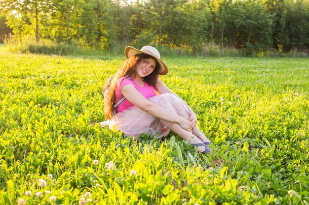 Schöne junge lachende freche Frau, die auf dem Gras sitzt und lächelt