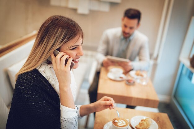 Schöne junge lächelnde Frau, die Smartphone benutzt und Kaffee in einem Café trinkt. Selektiver Fokus. Fokus auf Geschäftsfrau.