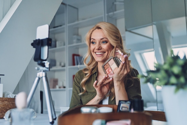 Schöne junge lächelnde Frau, die über Make-up- und Schönheitsprodukte Vlogging