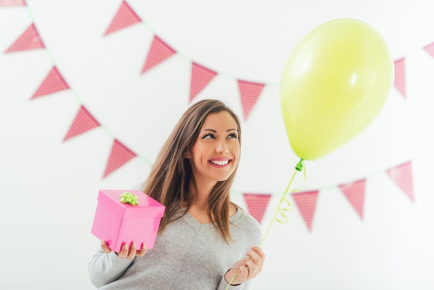 Schöne junge lächelnde Frau mit rosa Geburtstagsgeschenk und Ballon.