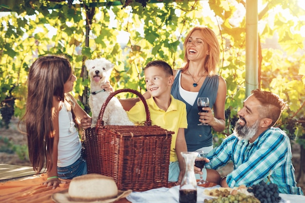 Schöne junge lächelnde vierköpfige Familie mit Hund beim Picknick auf einem Weinberg.