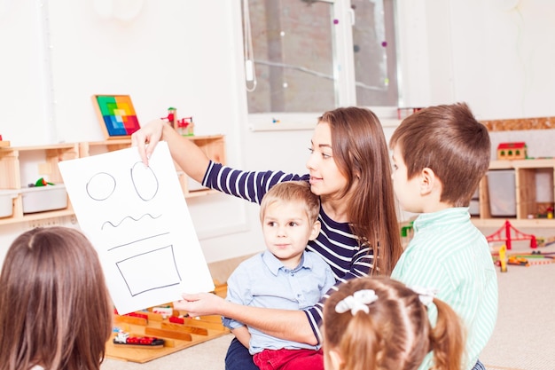 Schöne junge Lehrerin, die Figuren im Vorschulalter zeigt, Kinder sitzen im Kreis